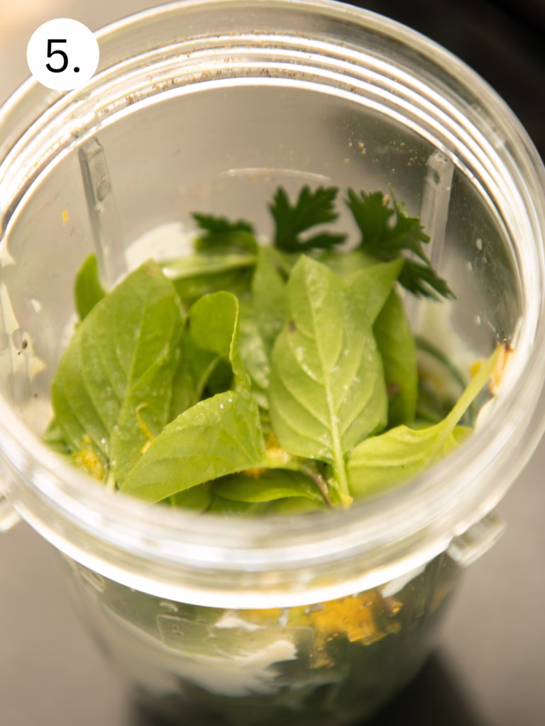 Fresh basil and parsley added to a blender cup to make homemade Green Goddess dressing.