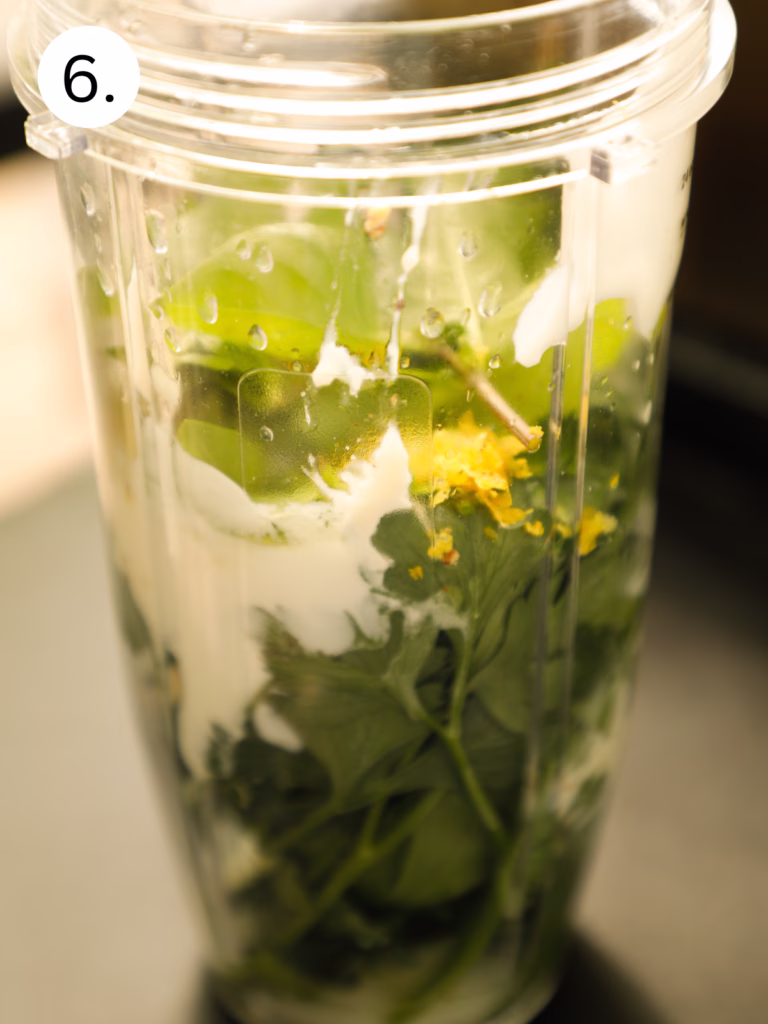 Blender filled with yogurt, herbs, garlic, lemon, mustard, anchovy paste, and seasonings before blending into Green Goddess dressing.
