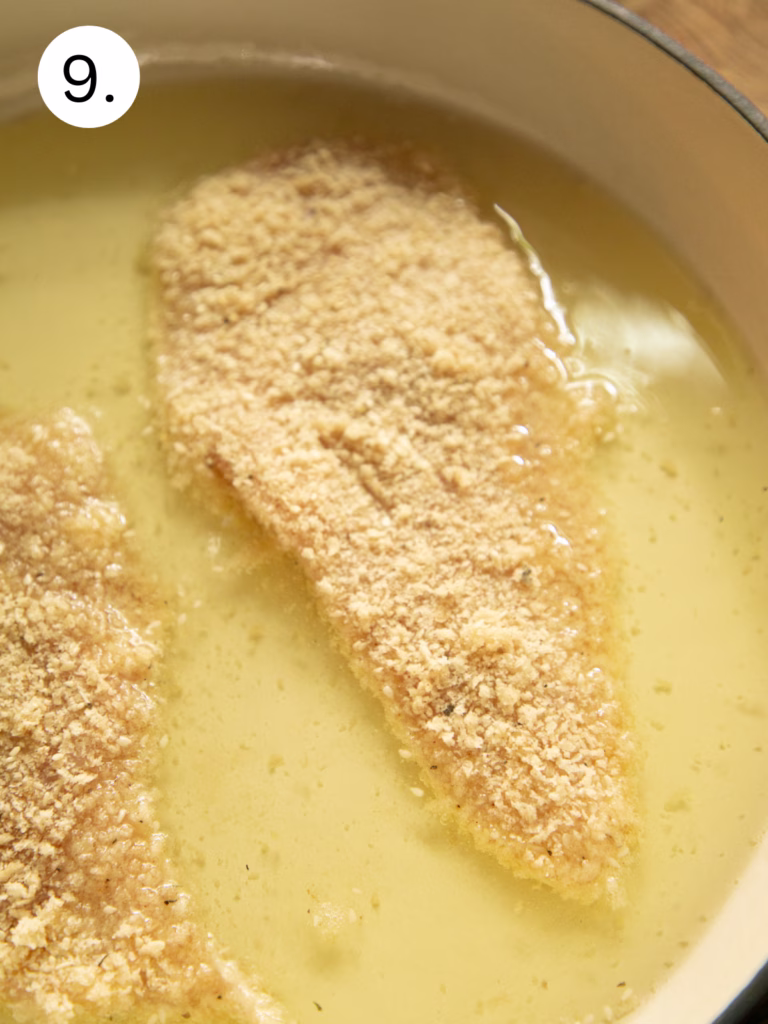Breaded chicken cutlets frying in hot oil in a Dutch oven, creating a crispy golden sesame crust.