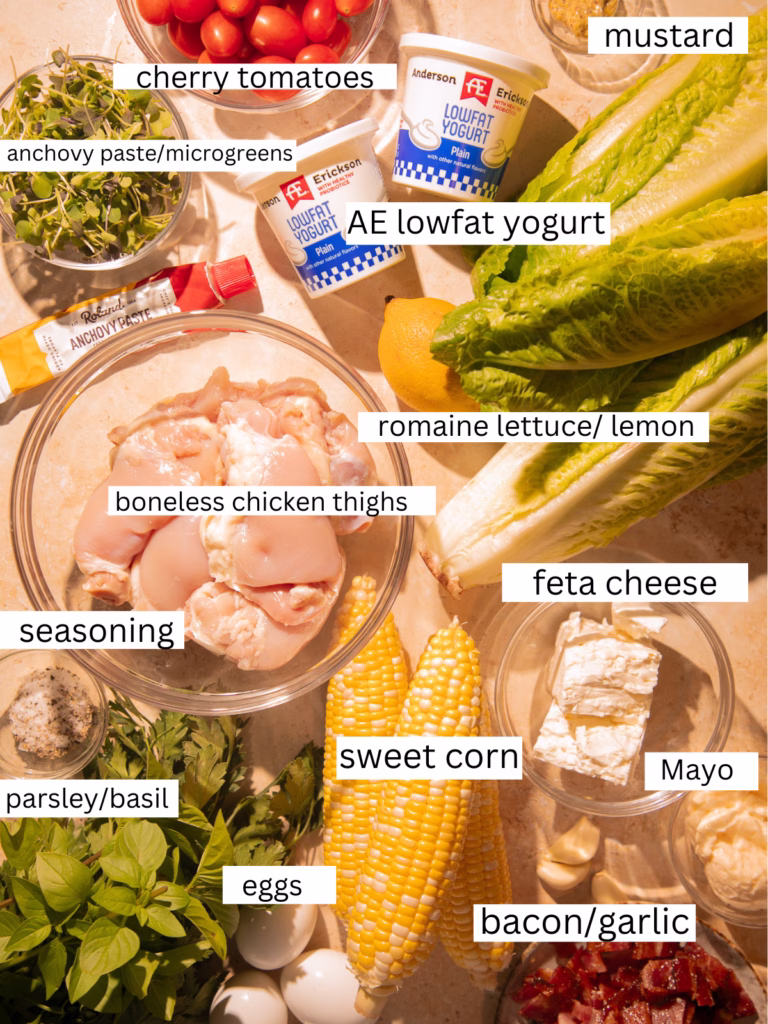 Ingredients for Grilled Green Goddess Cobb Salad including romaine lettuce, grilled chicken thighs, sweet corn, cherry tomatoes, bacon, eggs, feta cheese, fresh herbs, low-fat yogurt, garlic, lemon, mustard, anchovy paste, and seasonings.