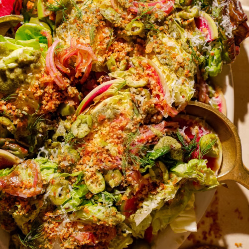 Close-up of a little gem lettuce salad featuring watermelon radish slices, Castelvetrano olives, fresh dill, Parmesan cheese, marinated red onions, and grilled spring onion dressing.