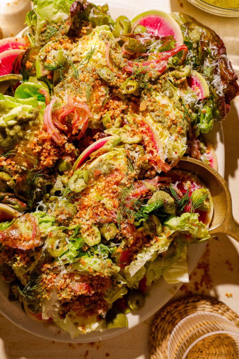 Close-up of a little gem lettuce salad featuring watermelon radish slices, Castelvetrano olives, fresh dill, Parmesan cheese, marinated red onions, and grilled spring onion dressing.